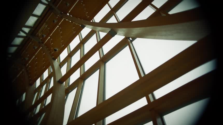 Architectural structure with curved wooden beams and large glass windows viewed from a low angle