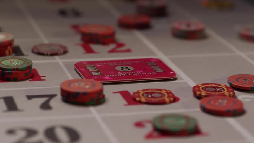 Casino roulette table with various colored chips while a croupiers hand collects bets