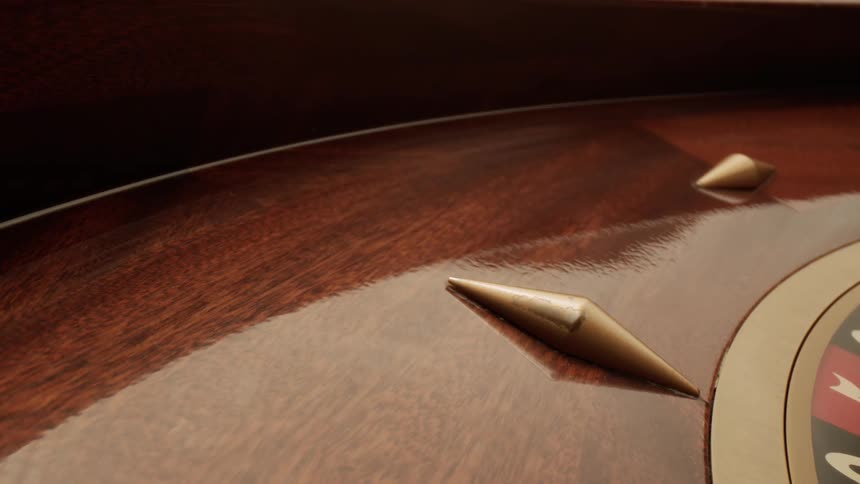Closeup of the rim of a casino roulette wheel shows polished wood details and gold pins