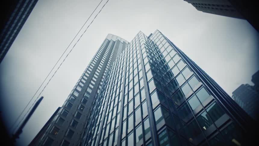 A low angle shot of two tall modern buildings with glass facades reaching towards a cloudy sky creating a sense of height and architectural grandeur