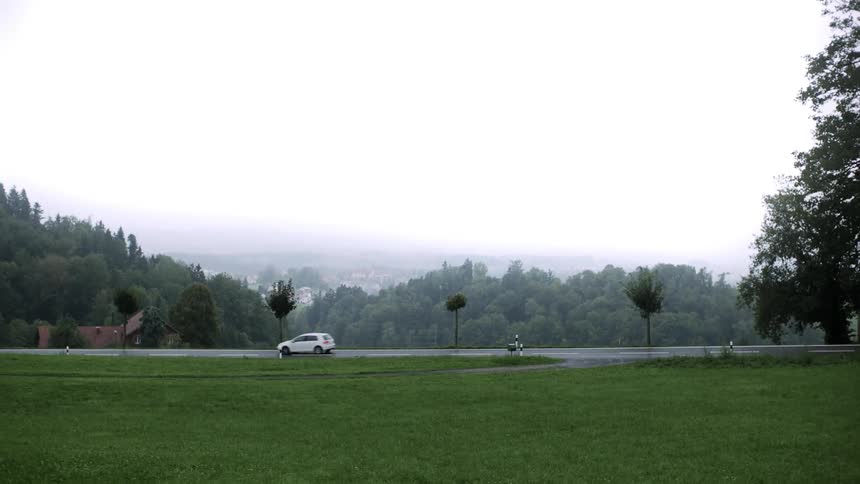 Landscape of a grassy field next to a highway with vehicle traffic and a city in the fog on the horizon