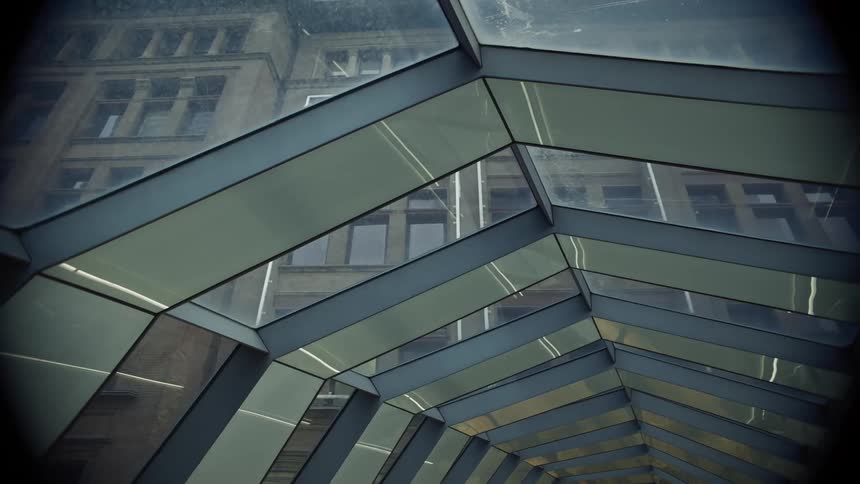 Glass walkway with geometric structure reflects the facade of a historic building