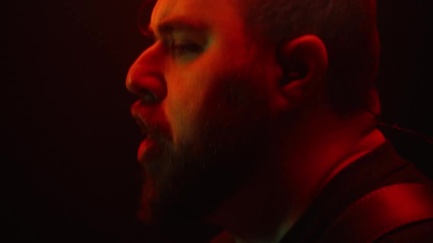 The face of a man who is screaming and he is in a dark environment with lights reflecting on his face