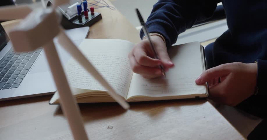 A girl is writing notes by her laptop