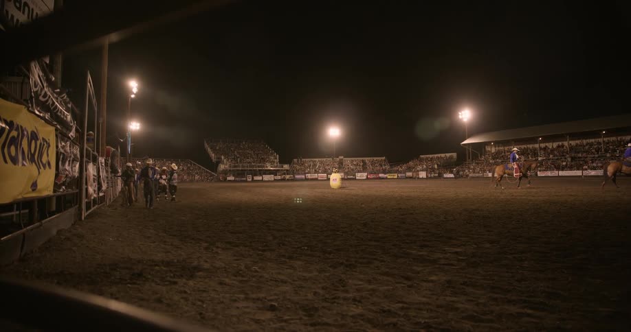 Rodeo arena lit up at night with a mounted rider and spectators in the stands