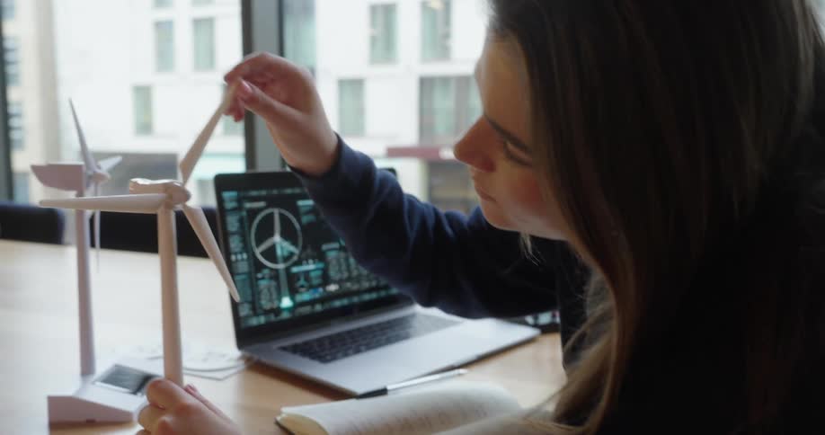 Woman interacts with a wind turbine model while analyzing data on a laptop
