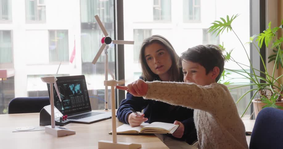 Young woman and a boy interacting with model wind engine propellers on top of an office desk