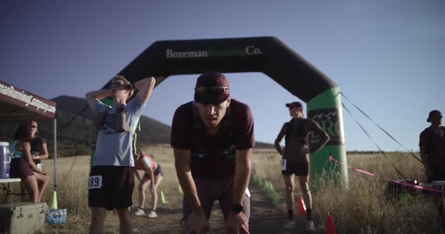 A small group of runners cross the finish line in a remote grassland on a sunny day