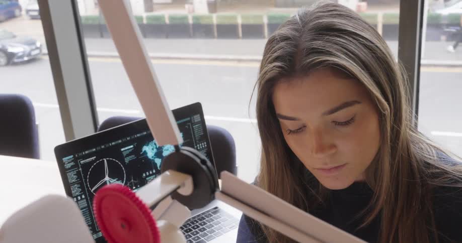 Young woman interacting with a wind power prototype and taking notes in a notebook