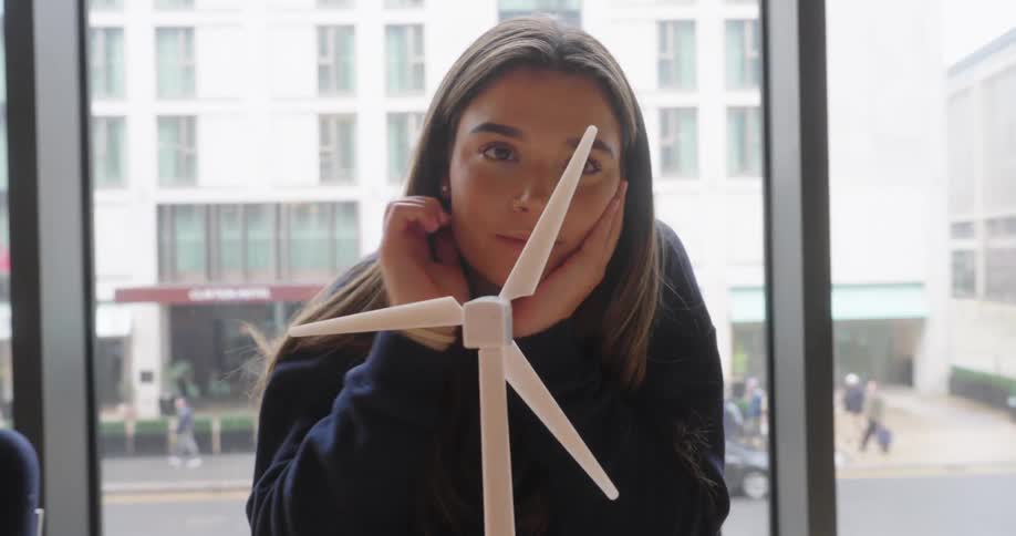 Woman observes and rotates a model wind turbine with her fingers