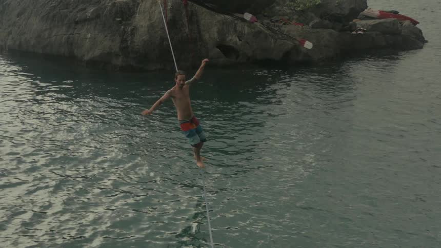 A man balances on a tightrope and then falls into a body of water
