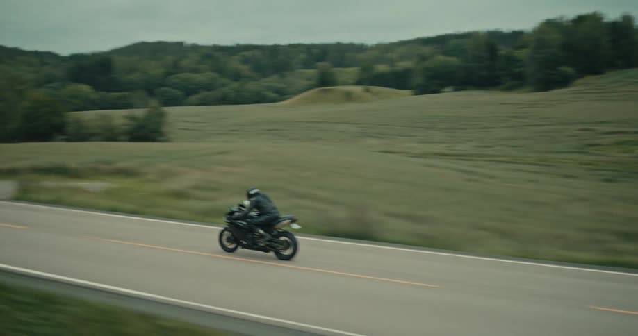 Motorcyclist rides along a highway passing through the forested and hilly countryside