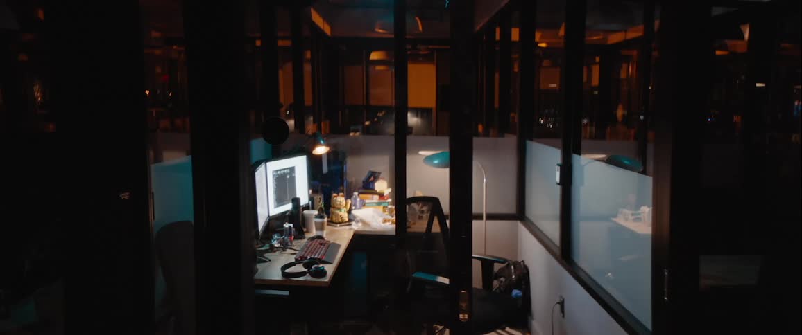Beckoning cat figure waves its arm from its position on a desk in a cubicle in a dark office building