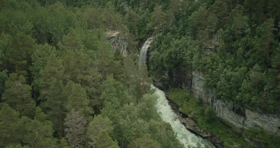A waterfall cascades into rapids of a river in a canyon