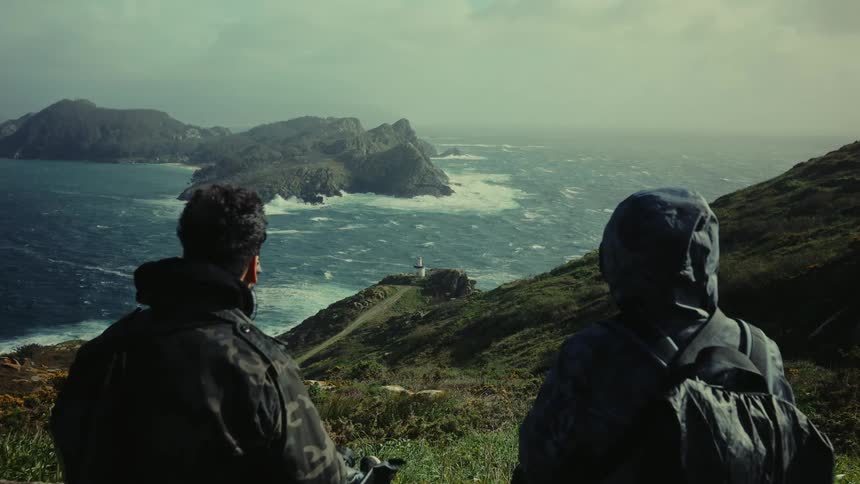 Two people sitting on a mountain peak enjoying the view of the ocean