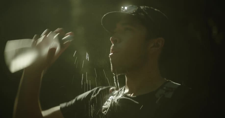 A runner pours water over his face letting it splash in the dim light before quickly taking off into a determined sprint