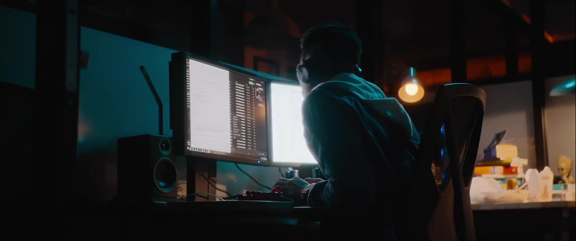 Man working in his office after hours leans forward to scan his computer monitors