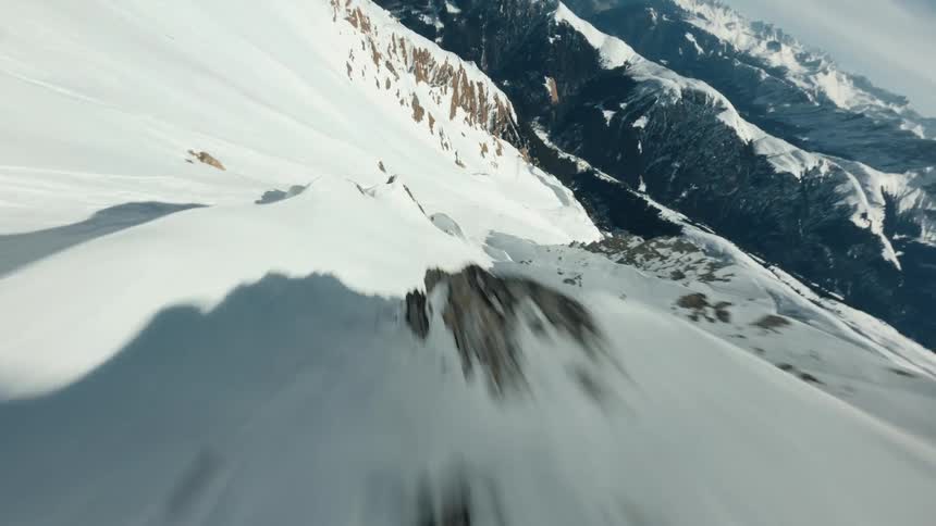 Aerial view of snow capped mountain peak with a distinctive rock spire at its summit set against a clear blue sky with a few scattered clouds