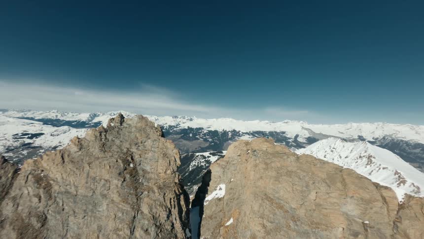 Flying towards a vast mountain range an aerial shot reveals two people standing on a snowcovered mountain peak as the camera orbits around them showcasing a breathtaking panoramic vista from a high altitude