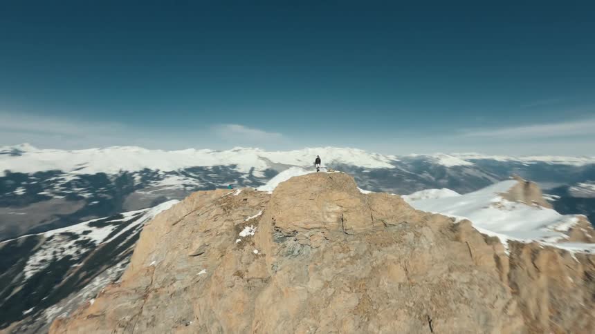 Man stands on a ridge overlooking a snowy mountain range on a winter day
