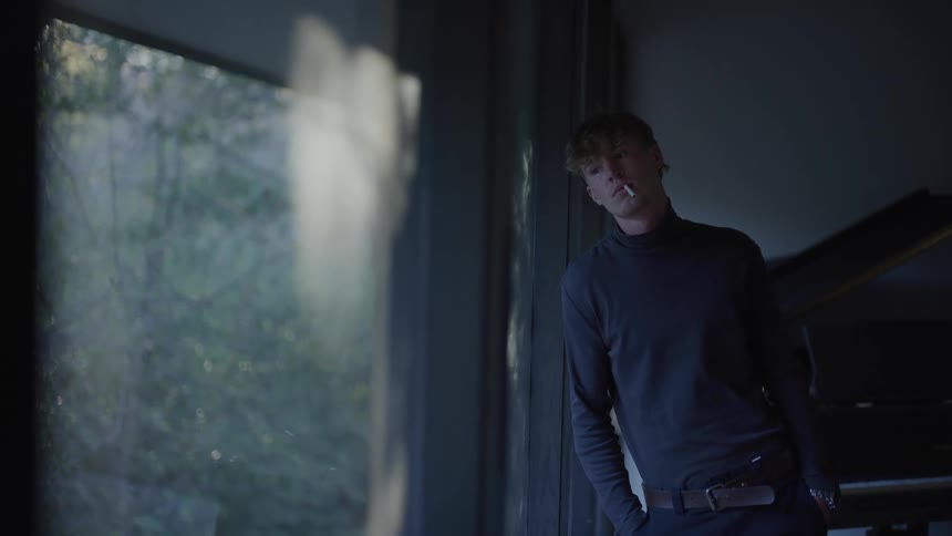 A man is leaning by the window with a cigarette