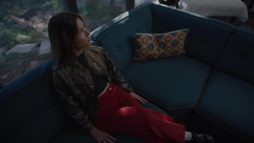 Woman sitting on a blue sofa looks to the side with natural light coming in through the windows in the background