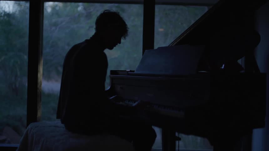 Seated person plays the piano in a dark room