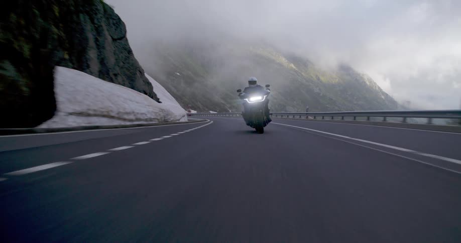 An adult rides a motorcycle up a mountain road on a foggy day