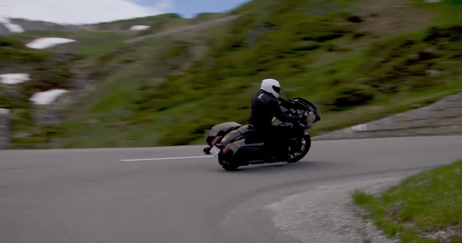 A person riding a highpowered motorcycle wearing a white helmet on an asphalt street in a region with mountains with a little snow covering them