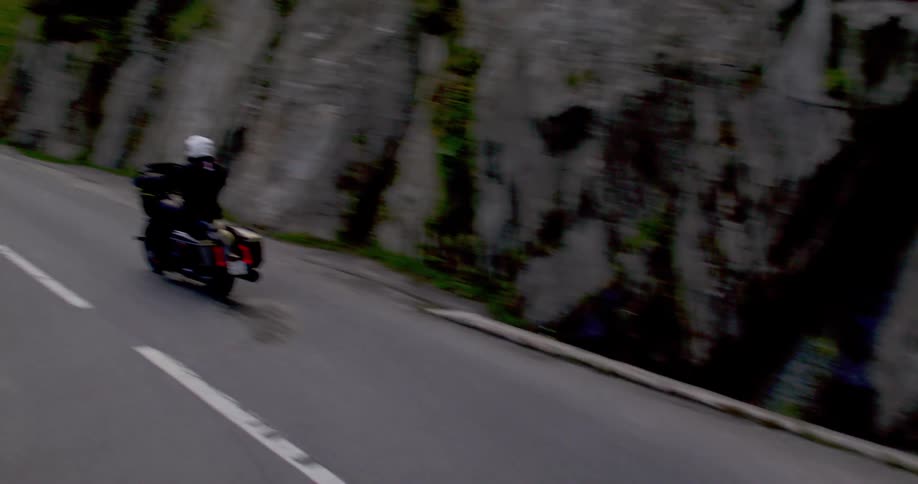 An adult rides a motorcycle through a sharp curve on a high mountain road