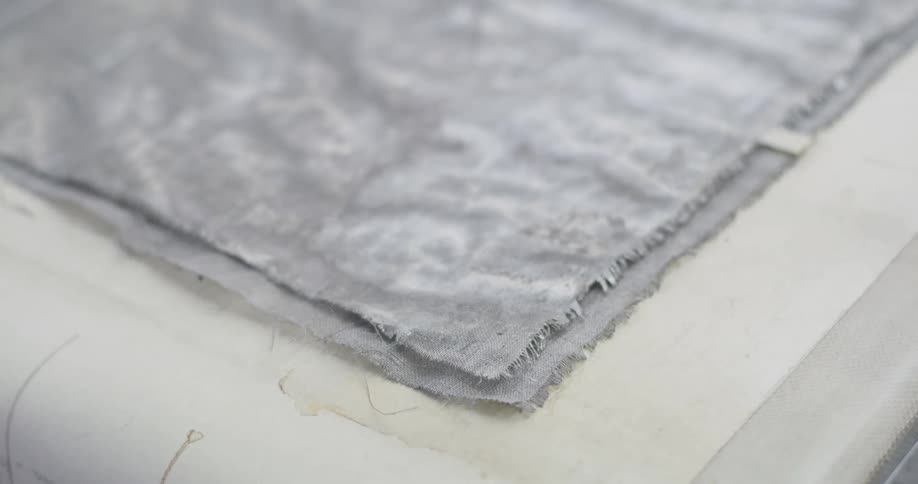 A gray cloth with two layers and the edges full of loose fibers on a white surface