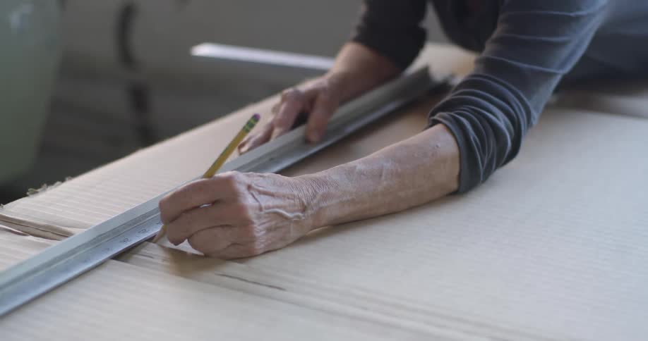 Woman uses a measuring stick to mark the piece of fabric lying on a work table in a workshop