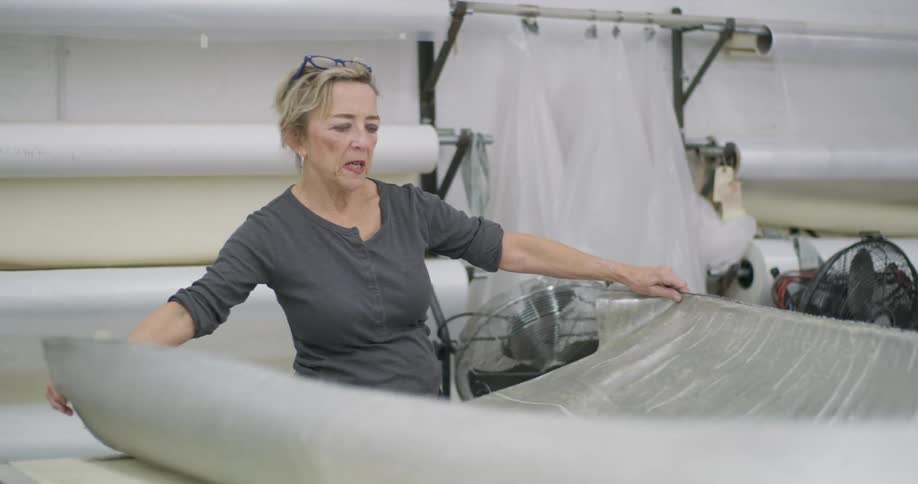 A blonde woman is unfolding a silver fabric while talking