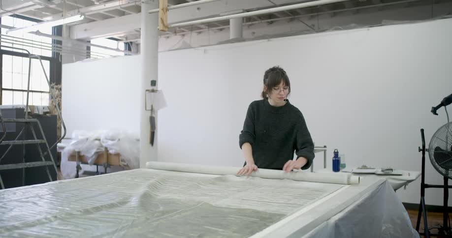 Woman unrolls a large piece of translucent fabric on a work table in a studio