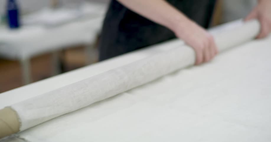 A person carefully rolls out a large sheet of fabric on a table preparing it for use in a technical project