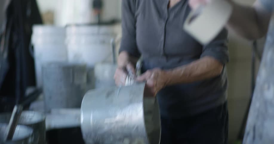 Two women are talking while in a workshop near some paint buckets