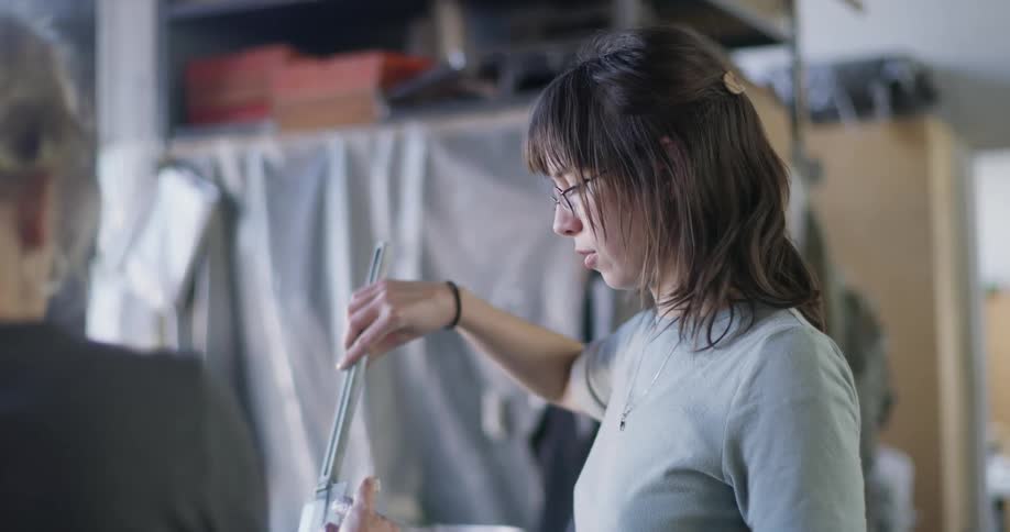 Woman talks to a coworker while stirring the contents of a bucket standing on a worktable
