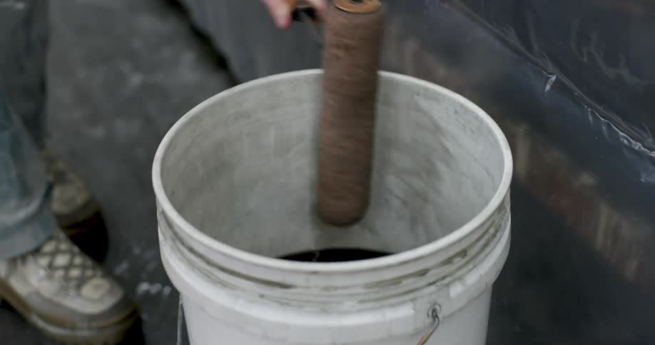 A woman rolls a roller on a table then moves it to a bucket