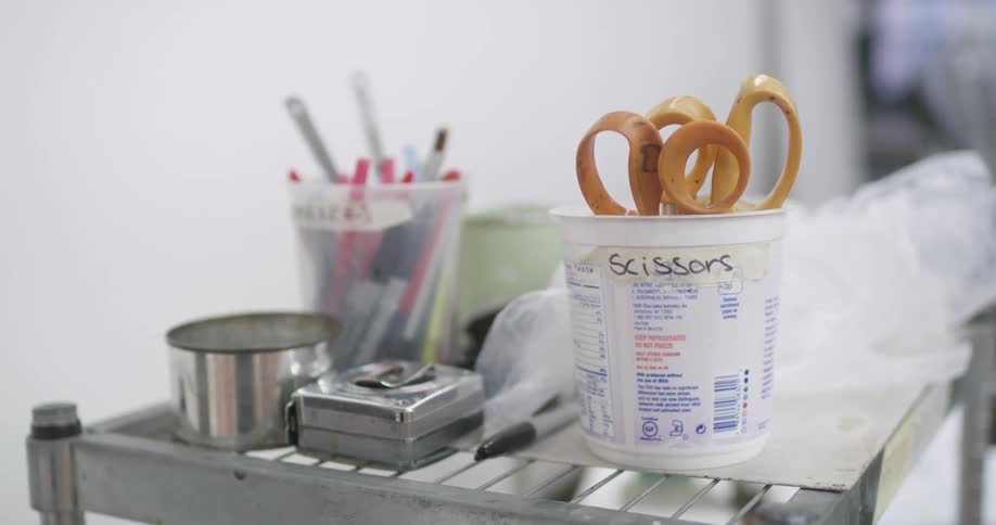 A container labeled for scissors stands on a metal cart among assorted art supplies capturing a simple yet creative workspace scene