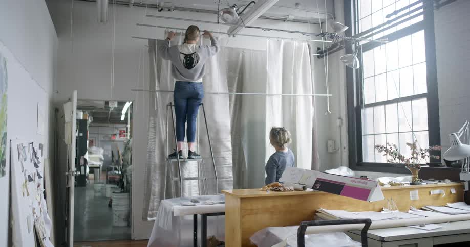 A woman is hanging curtains in a factory setting