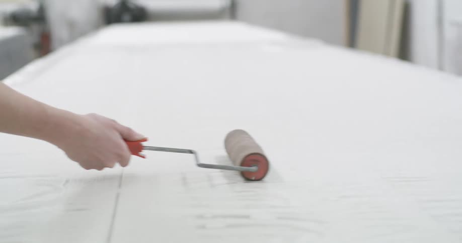 Two women painting a large table white using paint rollers