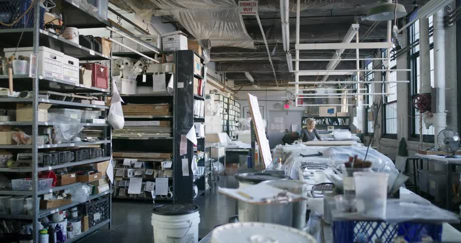 Spacious welllit art studio with shelves full of materials and a person working in the background