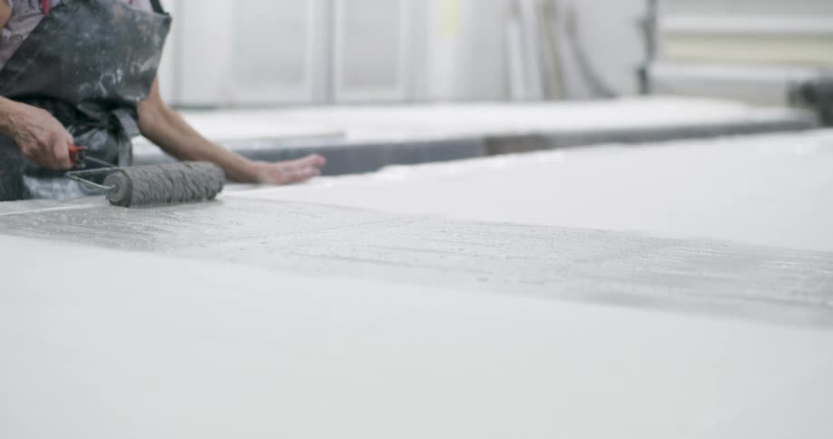 A woman uses a roller to transfer gray paint onto a large white surface
