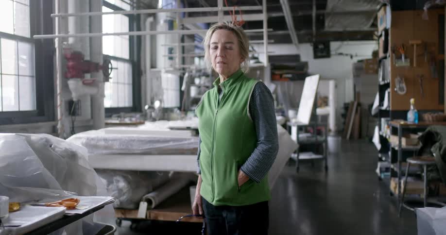 A woman is standing in a room with fabric and sewing machines