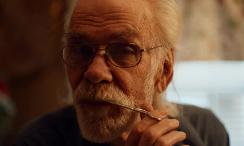 Portrait of an elderly man trimming his beard with small scissors