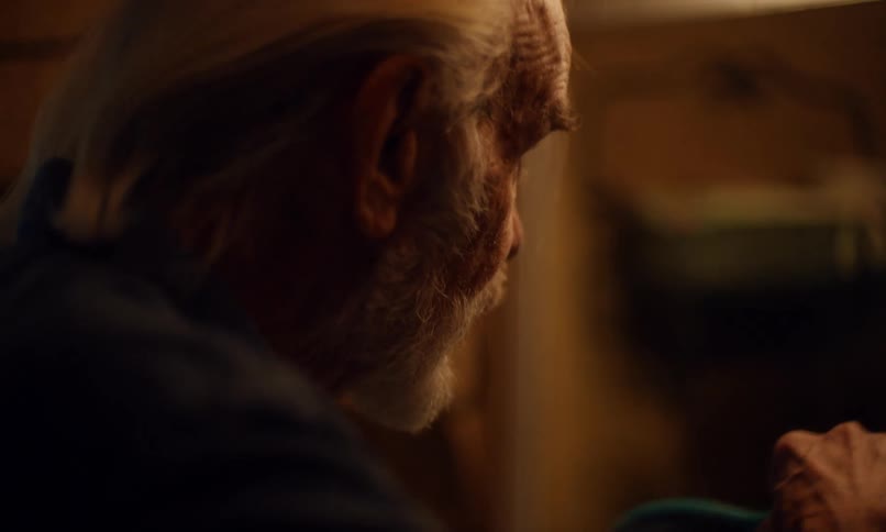 In a dimly lit room an elderly gentleman is carefully grooming himself as captured in a closeup shot focused on the deliberate action of brushing his distinguished silver hair with a bluehandled brush showcasing a moment of quiet personal care