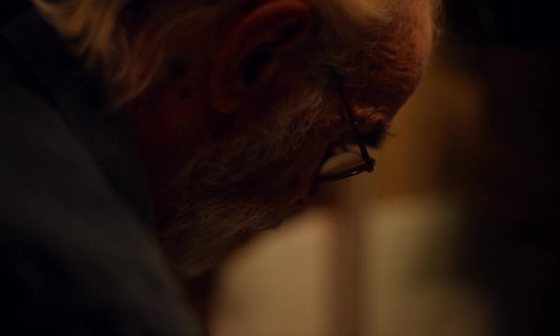 In a dim bathroom an older man brings a small paper cup to his mouth swishing liquid as if rinsing before spitting it out of view