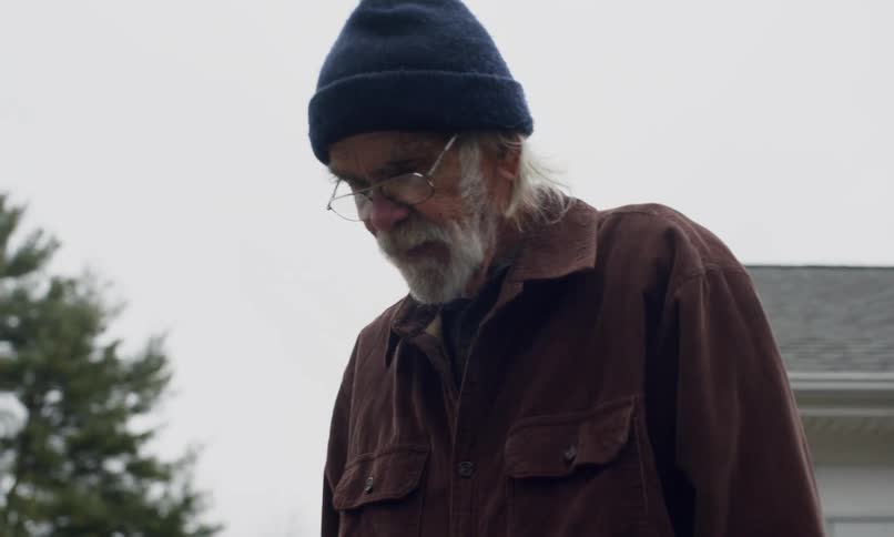 Elderly man stands in a backyard on a cloudy day