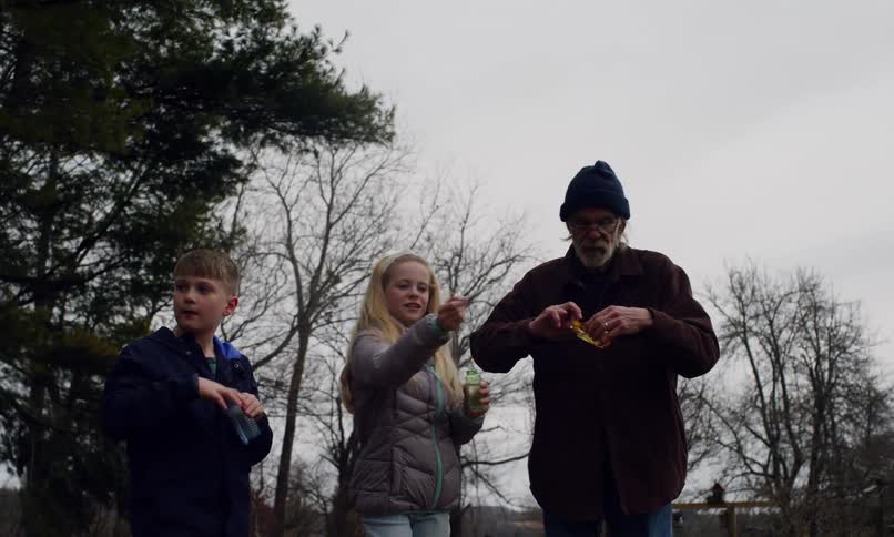 Grandfather blowing soap bubbles with his two grandchildren outdoors