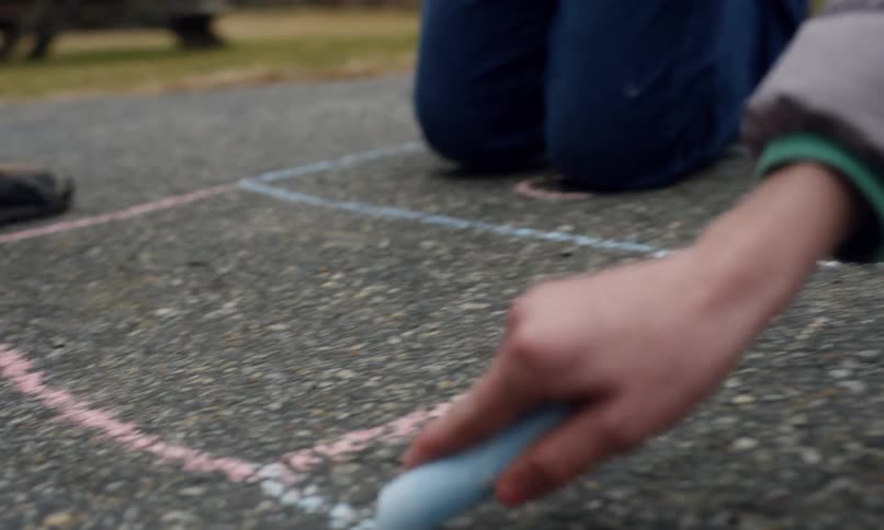 Two people draw a hopscotch grid on asphalt with chalk